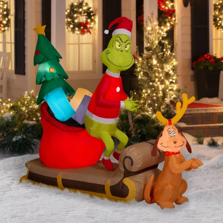 Grinch and Max on a sled Christmas inflatable, inflated in front of an illuminated house.