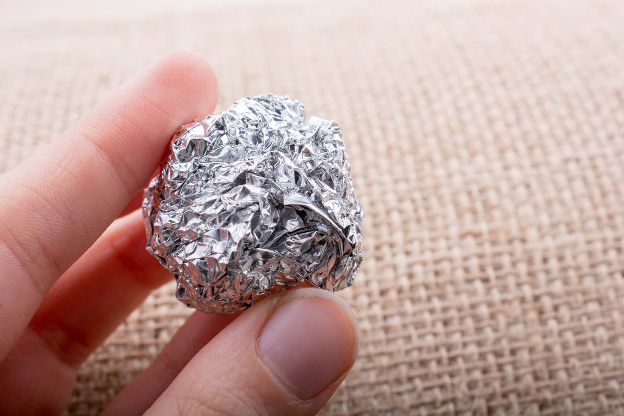 A-hand-holds-a-small-ball-of-aluminum-foil-against-a-cloth-background.