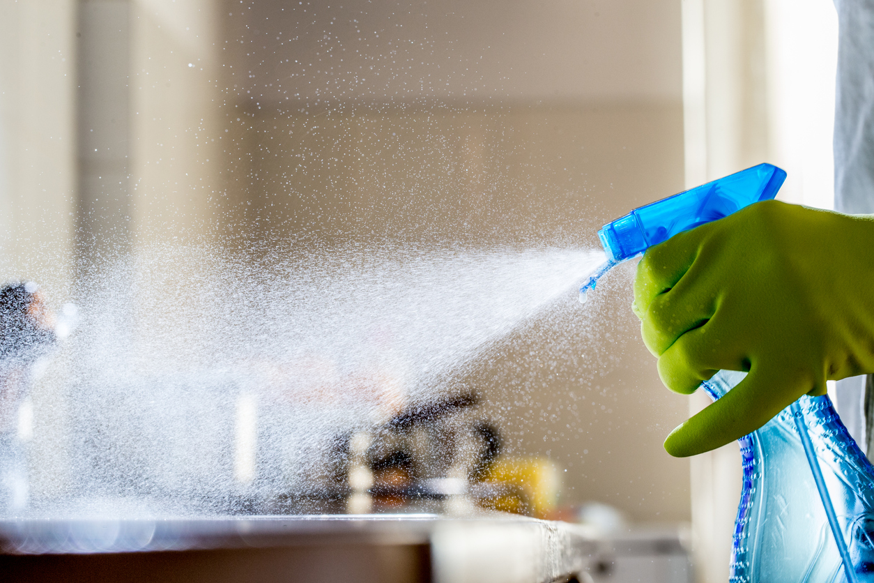 A-gloved-hand-sprays-blue-cleaning-product-onto-a-counter-surface.