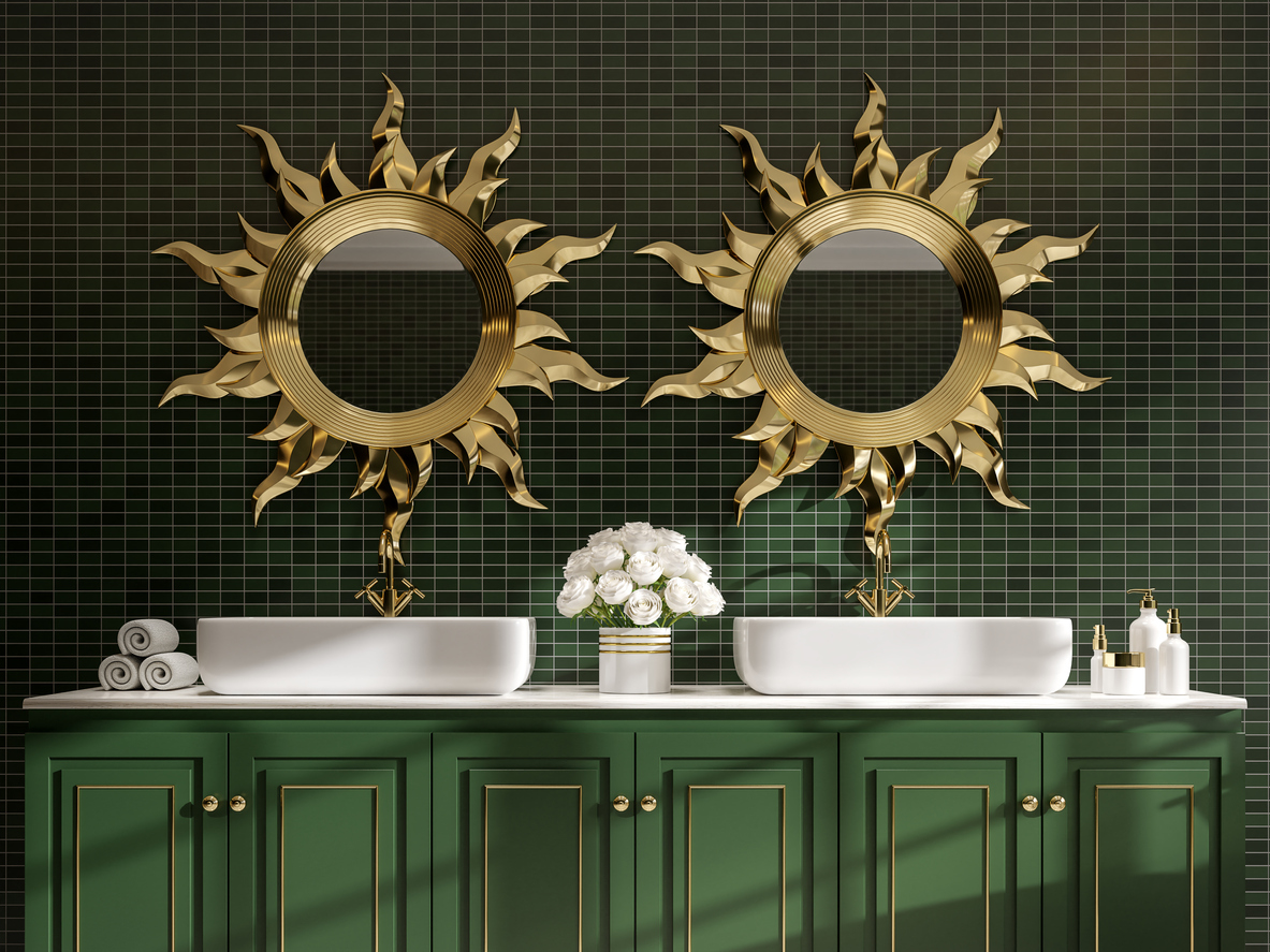 A-bathroom-with-dark-green-vanity-and-wall-tiles-is-decorated-with-gold-accents-and-sun-shaped-gold-frame-mirrors.