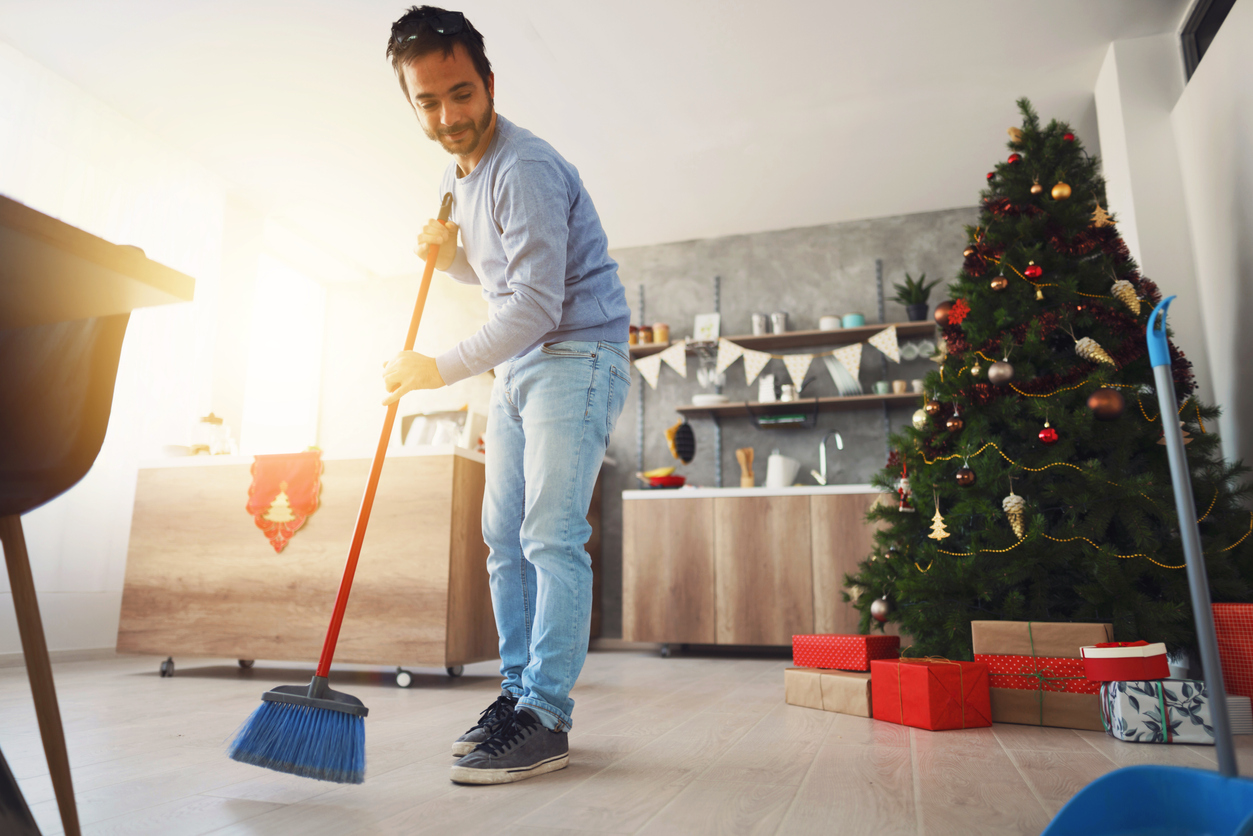 Mid adult man in a casual clothes sweeping floor with a broom and a dustpan at his home.