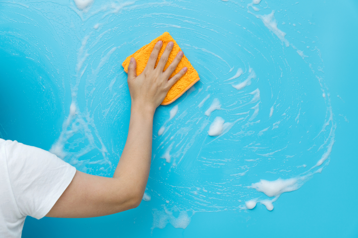 Woman with white shirt washes blue walls with yellow cloth and dish soap.