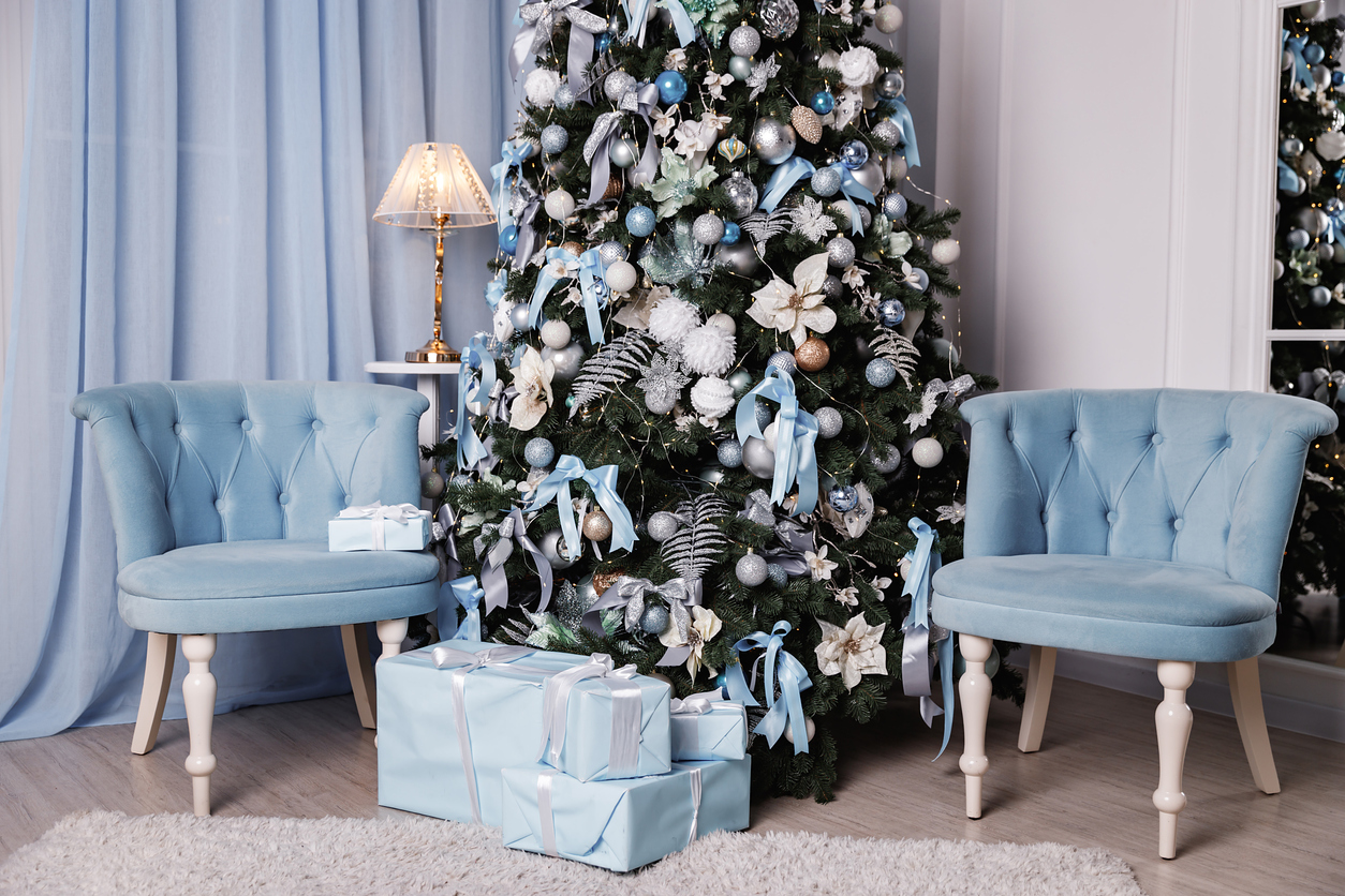 Christmas-tree-in-blue-and-white-theme-with-ribbons-and-floral-filler-branches-sits-between-two-blue-velvet-chairs.