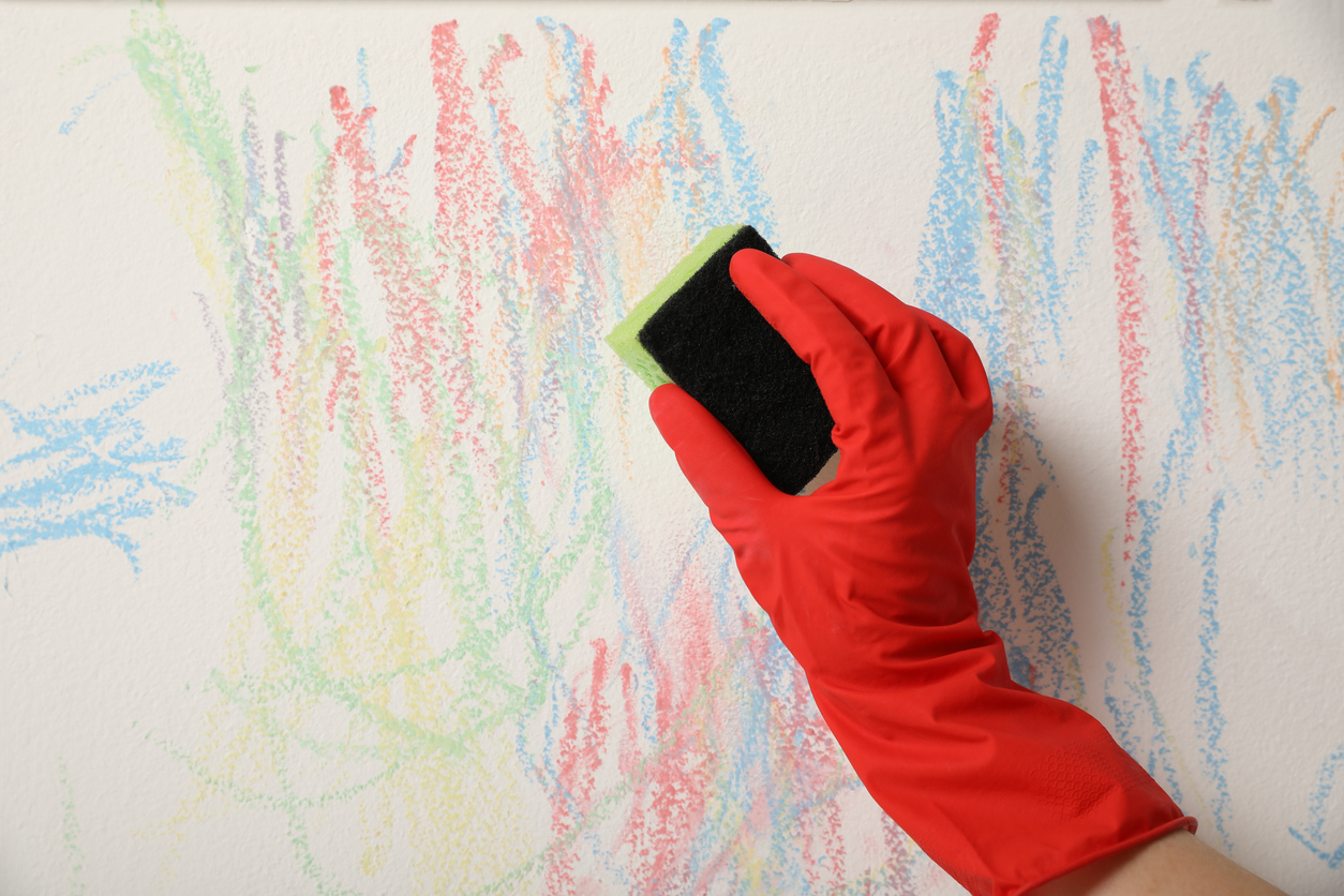 Hand with red gloves wipes off crayon from white wall with a sponge.