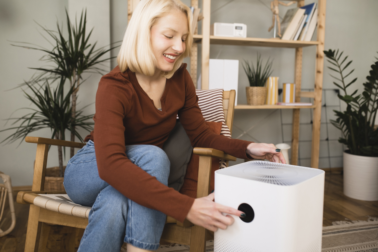 A woman turns on her air purifier while sitting in her living room.
