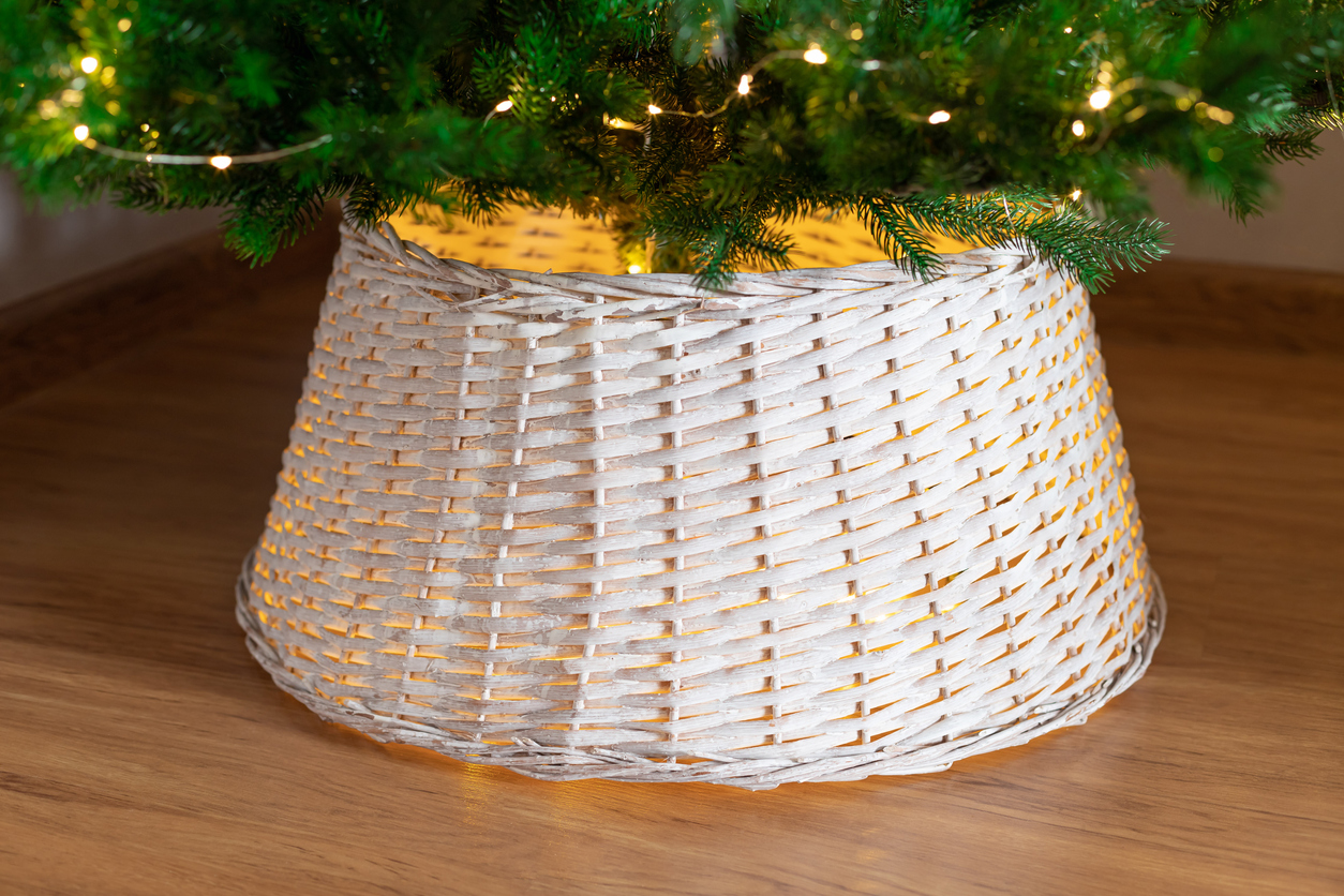The-base-of-a-Christmas-tree-sits-in-the-center-of-a-white-wicker-basket-collar.