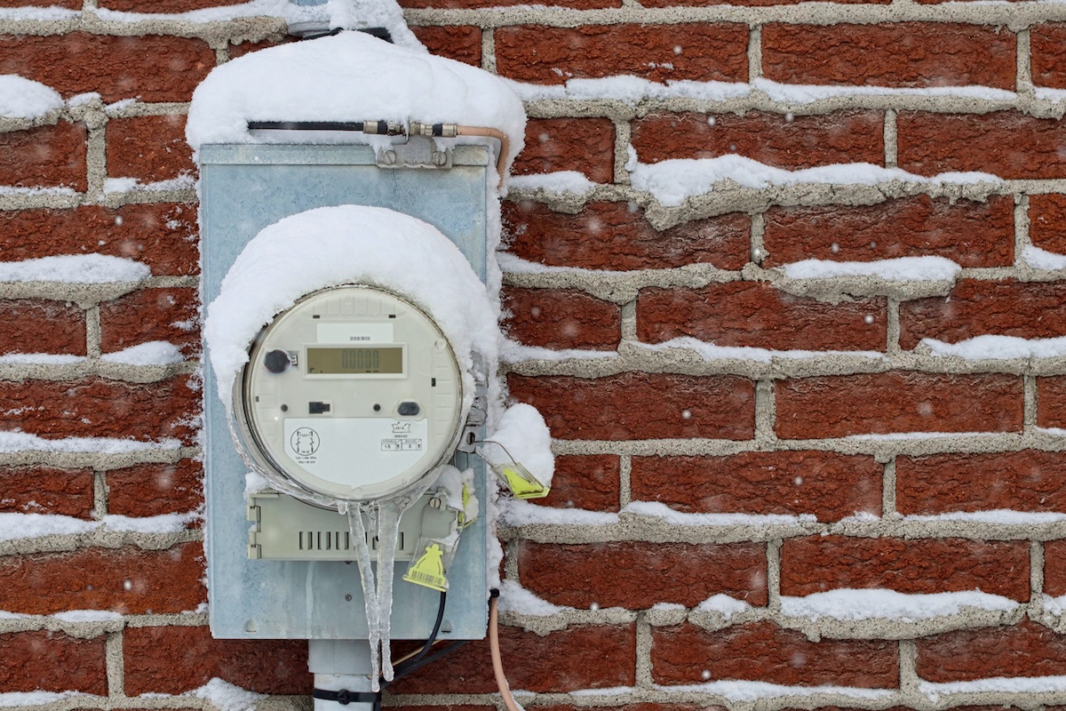 A home electric meter outside a brick exterior with snow on top.