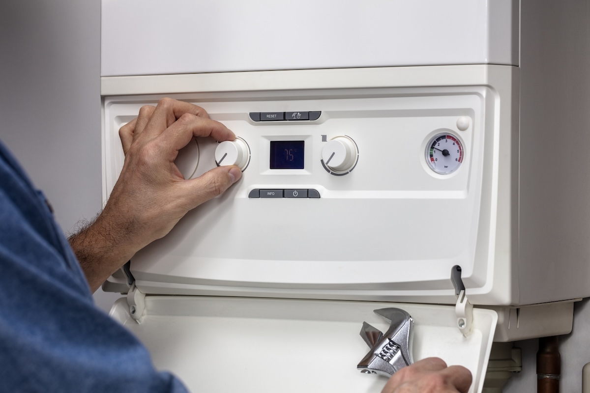 A plumber adjusts settings on a residential boiler system in a home.