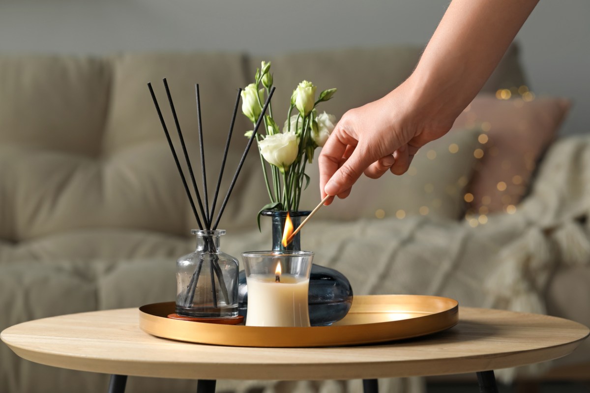 Woman lighting candle at wooden table in living room.