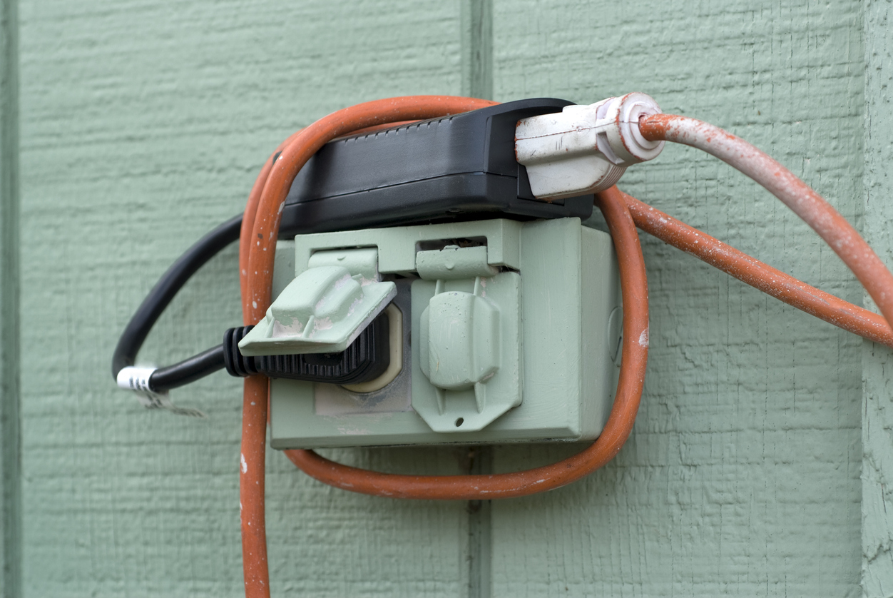 Closeup of an outdoor power outlet box on a (US) house with a cord plugged in.