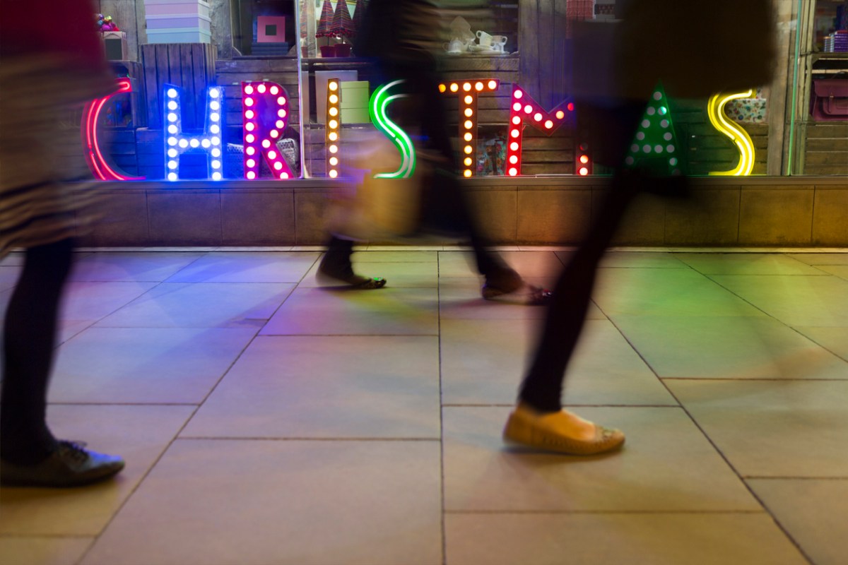 Peoples-legs-are-a-blur-as-they-walk-quickly-past-a-neon-sign-that-says-Christmas.