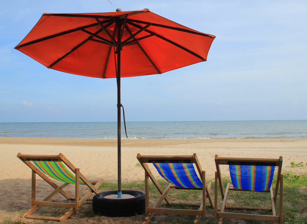 A beach with patio chairs on the sand with sun umbrella in a recycled tire stand.
