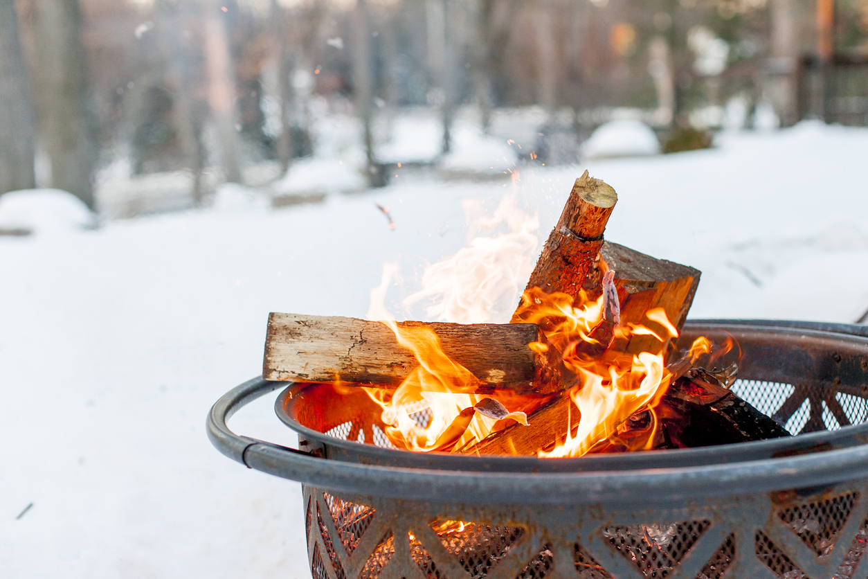 Bonfire close up during the winter season. Fire is inside a metal fire pit. Snowy scene and woods in the background.