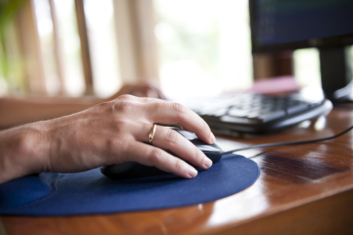 A person using a computer mouse on a mousepad on a desk in a home office.