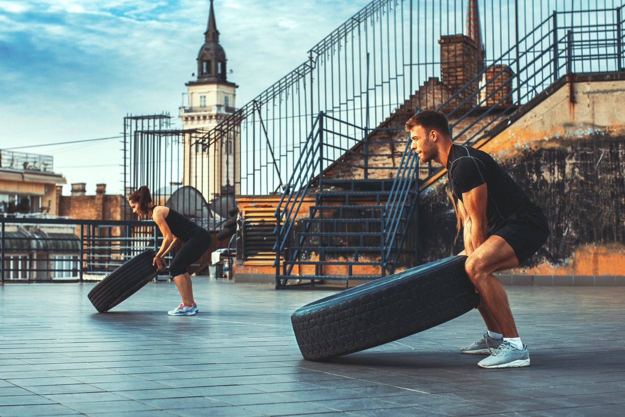 Young couple exercising on the roof of a building with tires
