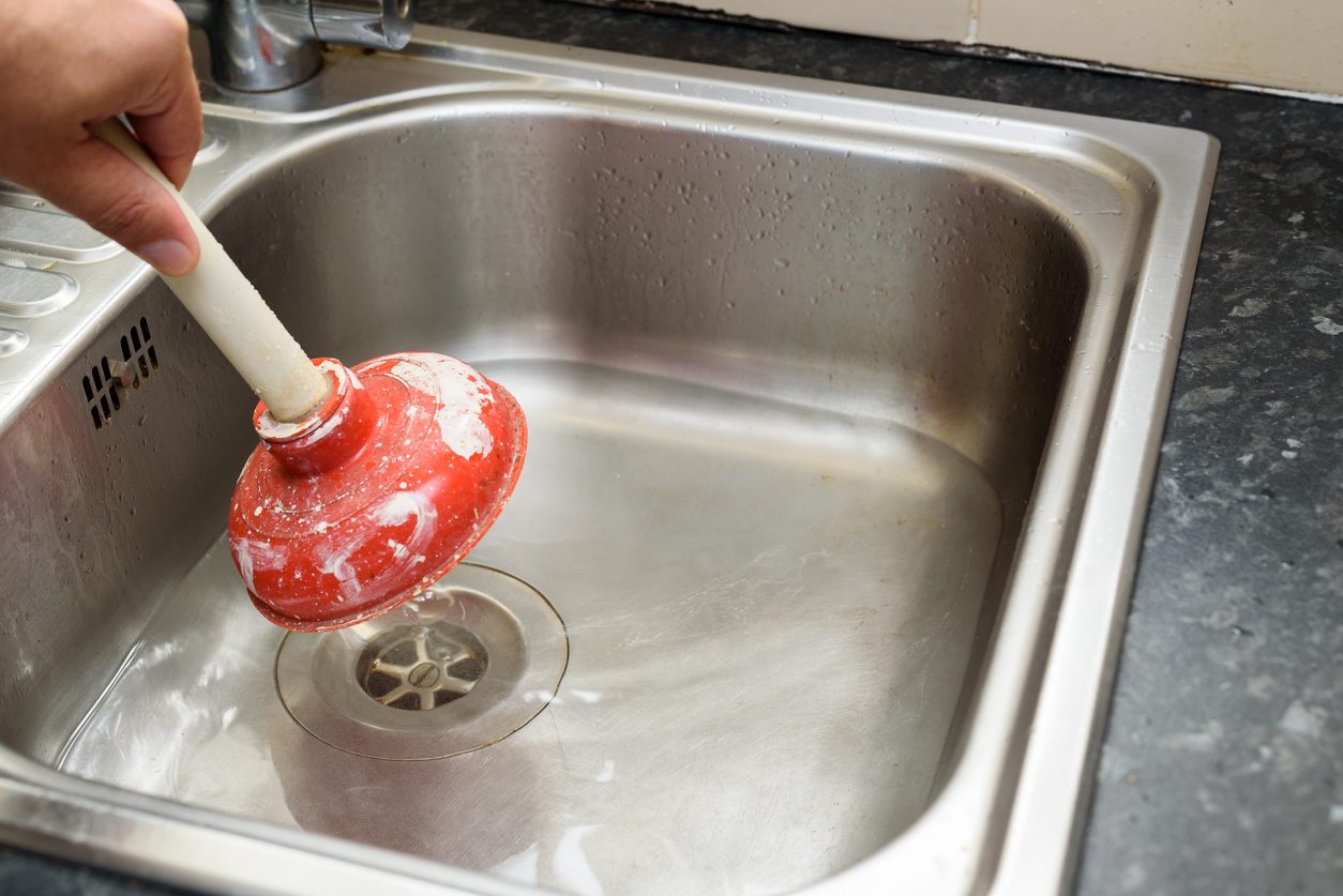 Man using a plunger with one hand and water in sink, used to clean a clogged / blocked kitchen sink