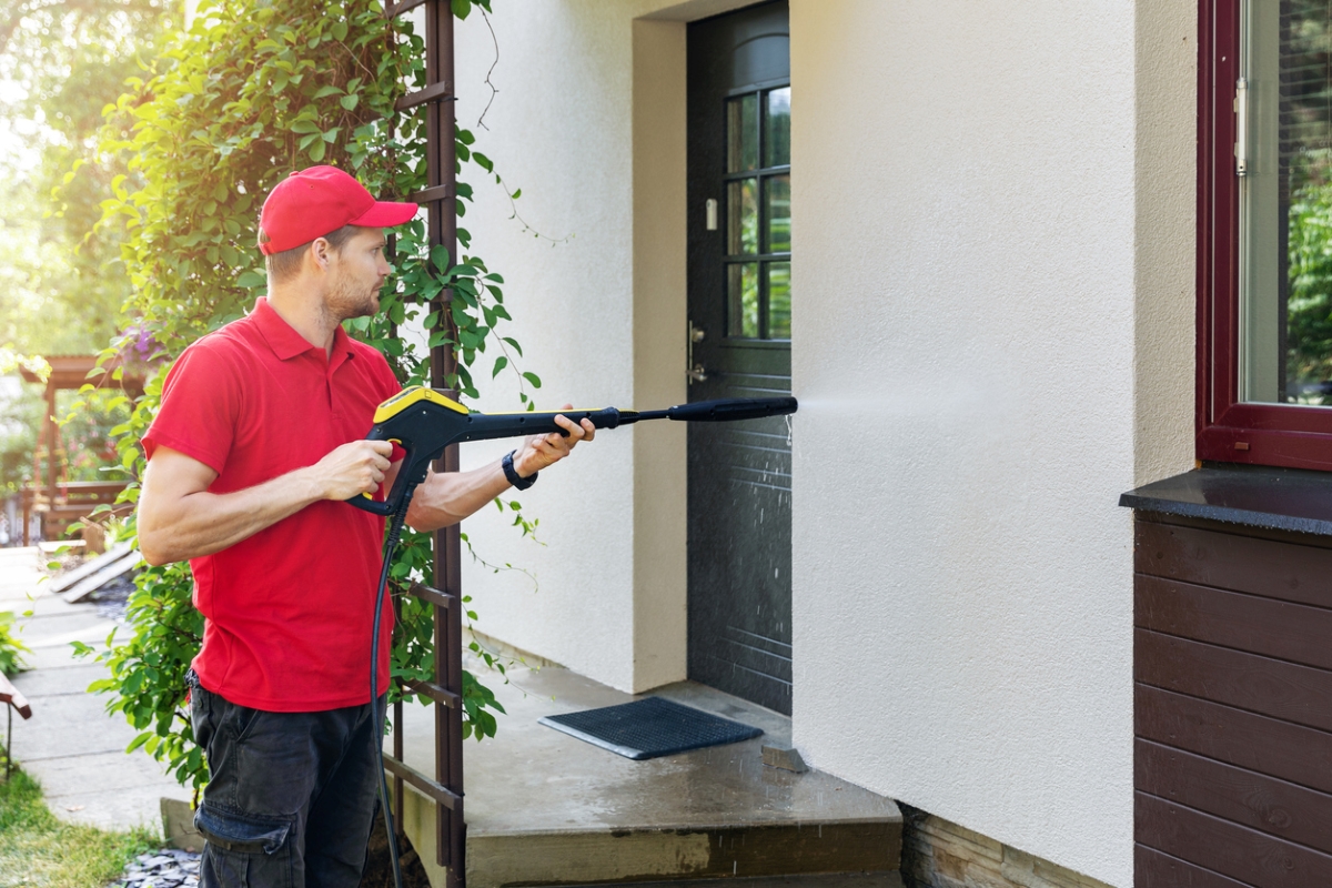 Man in red shirt and hat power washing house.