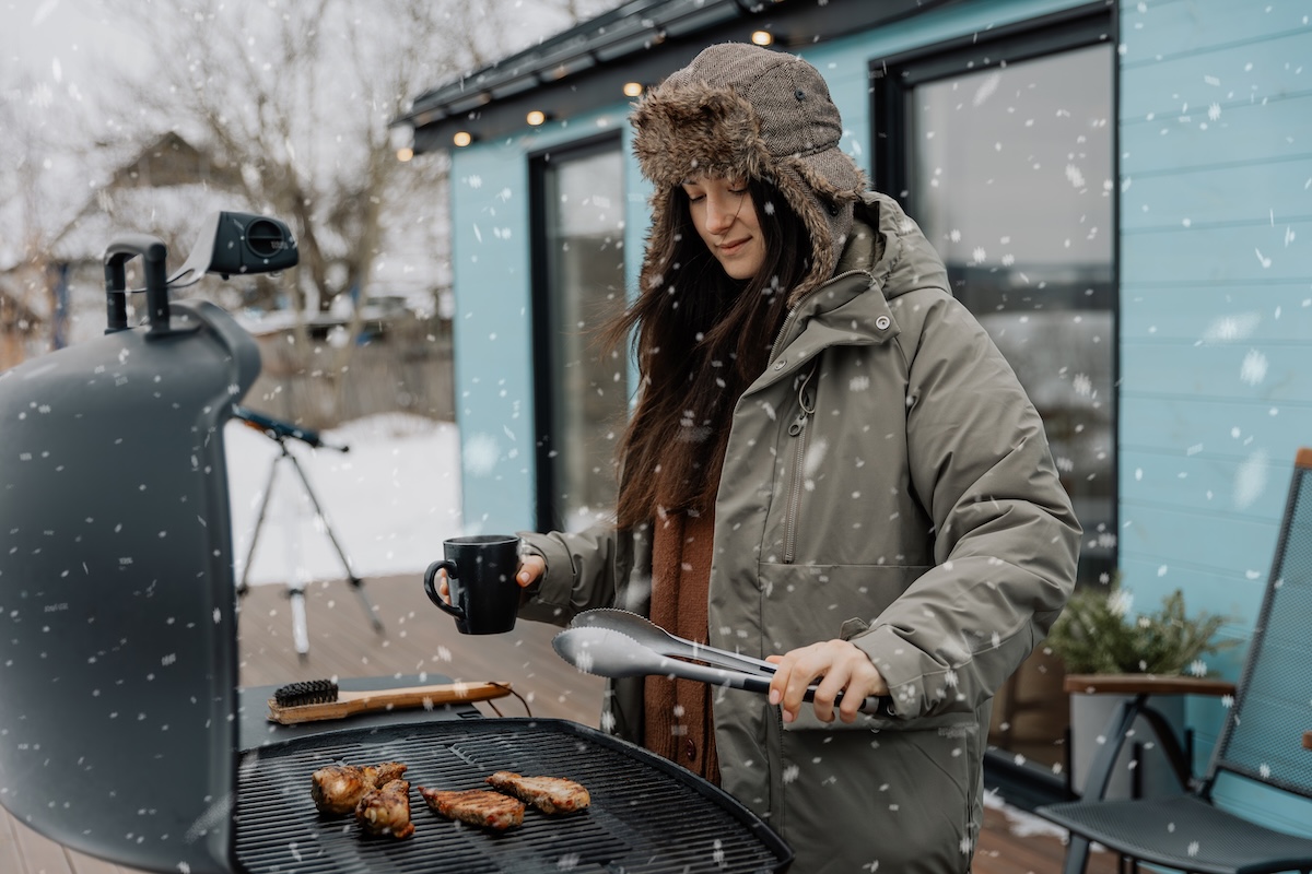 A young woman is grilling a barbecue outside her house in winter. 