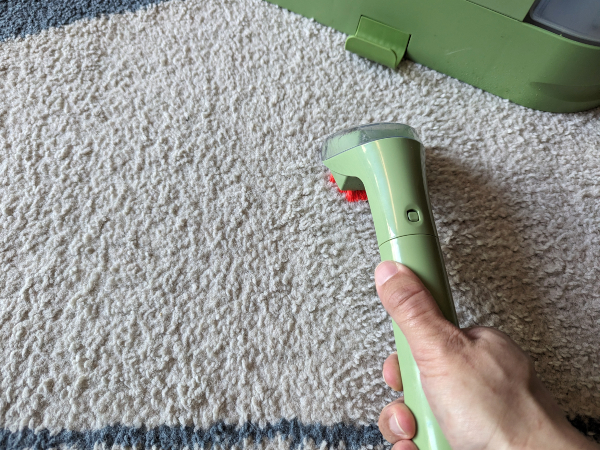 A blue-and-white area rug being cleaned with a Bissell Little Green carpet cleaner.