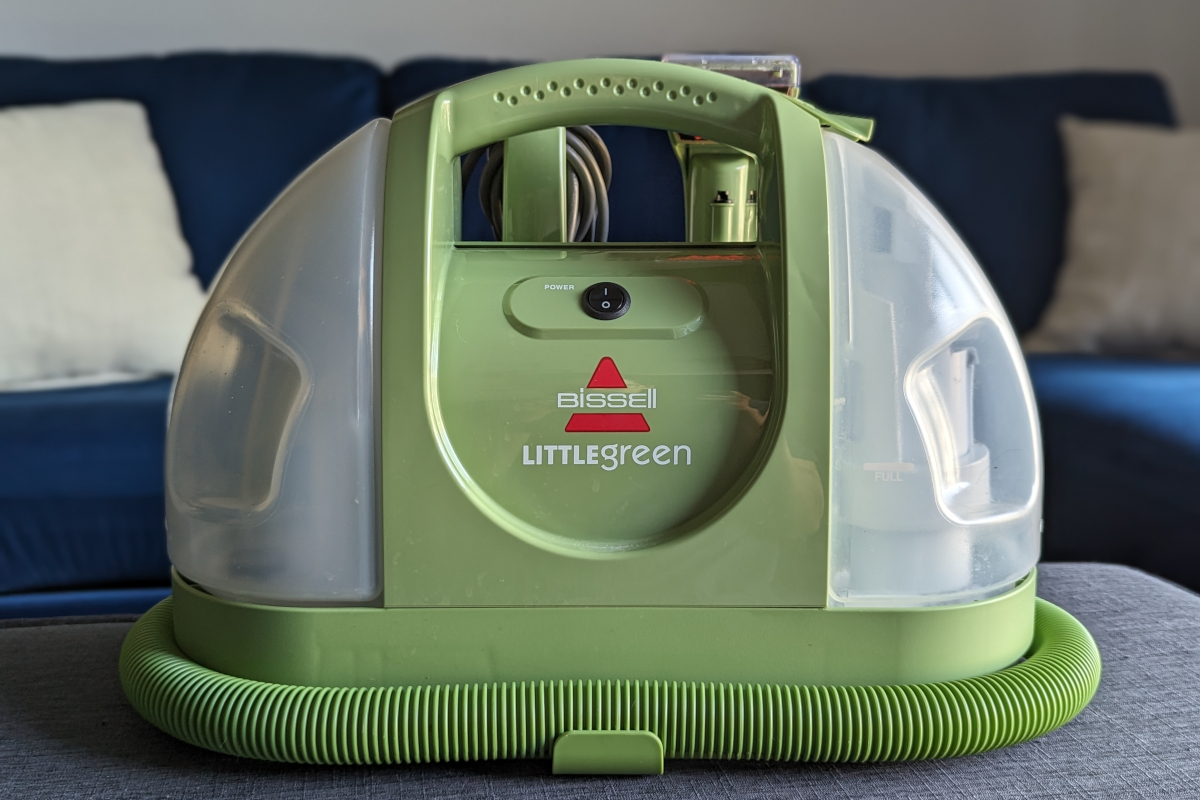 A Bissell Little Green portable carpet cleaner in front of a blue couch.