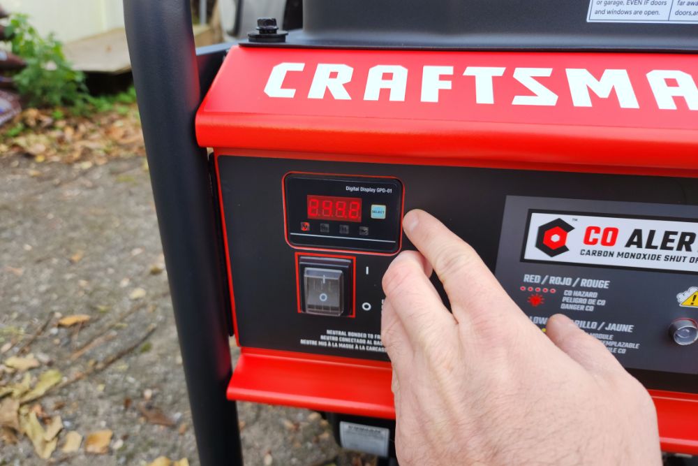 A person pointing to the digital display on the Craftsman 6000-watt generator during testing.