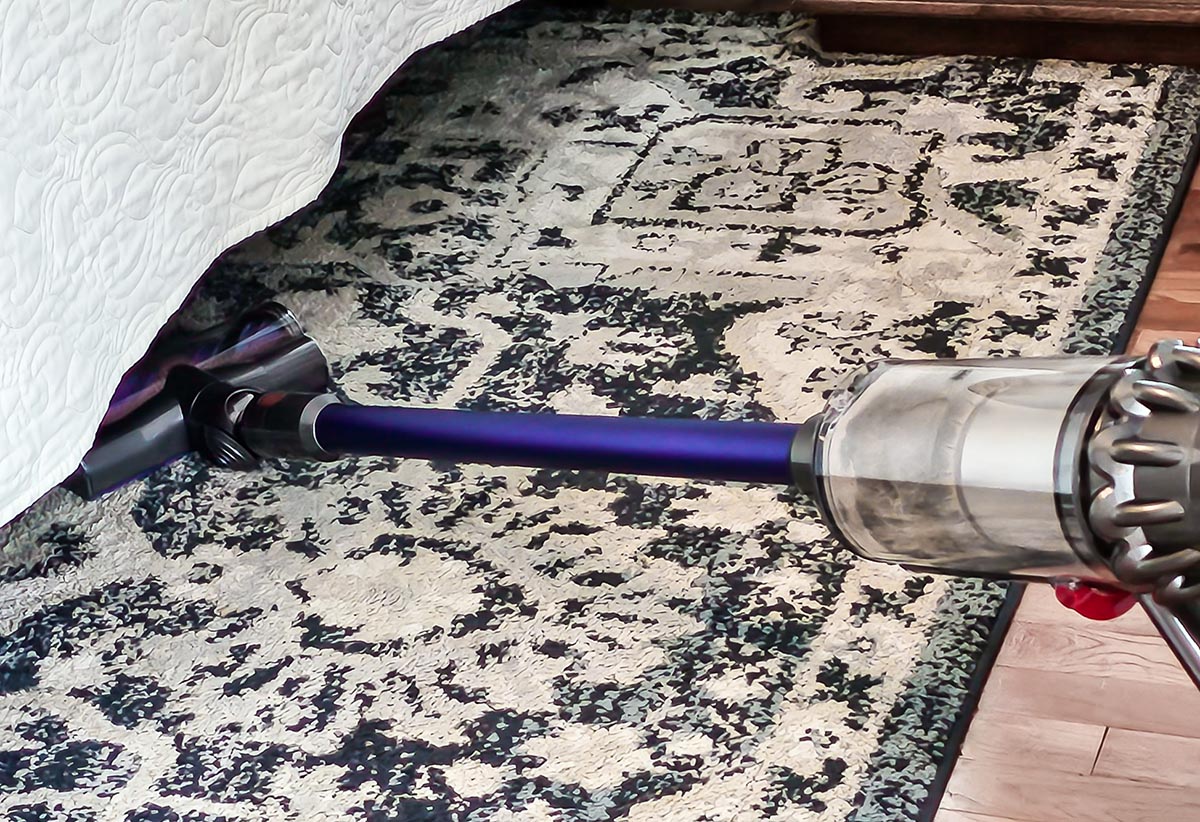 Person vacuuming black and white area rug under a bed with Dyson V15 Detect stick vacuum