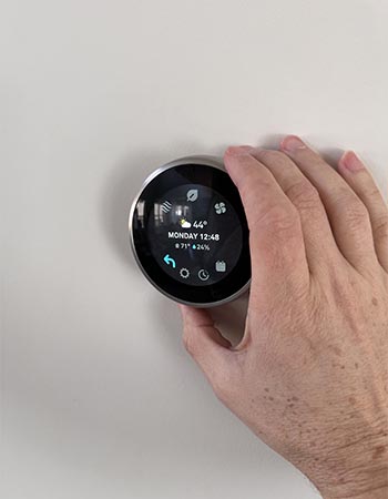 A person using the dial on the Google Nest Learning thermostat to manually adjust its settings during testing.