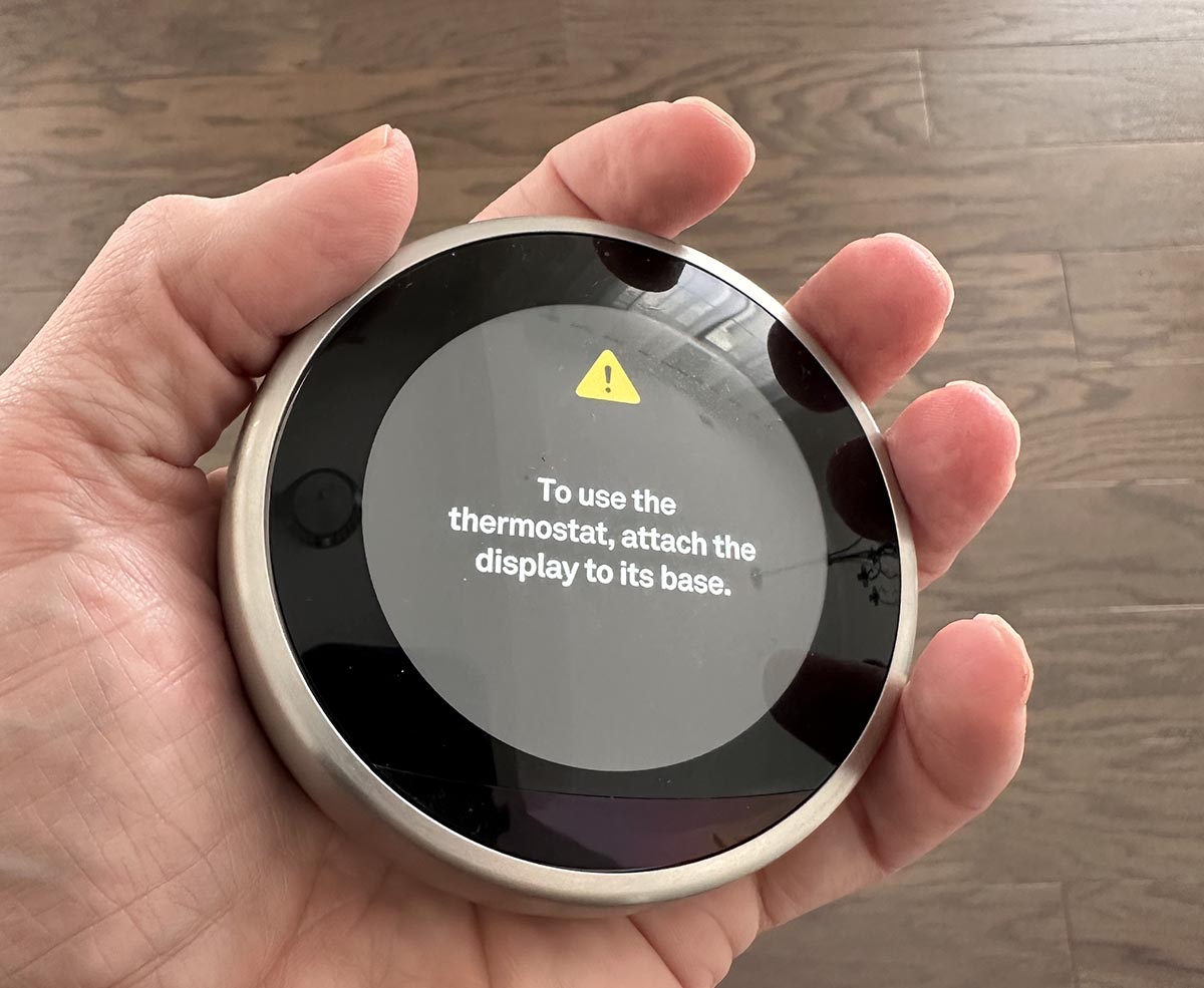 A person holding the Google Nest Learning thermostat during testing, which is small enough to fit in the palm of their hand.