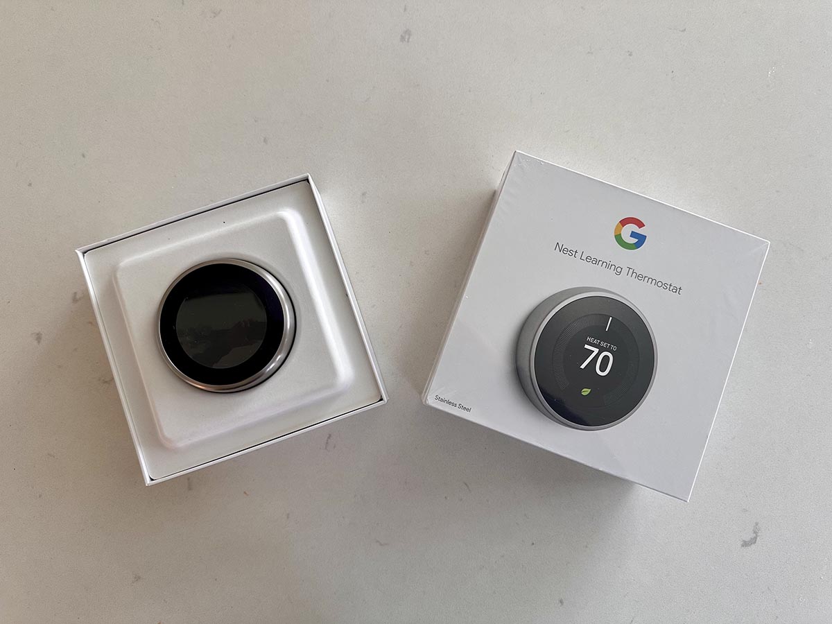 The Google Nest Learning Thermostat during unboxing with the product still in its white packaging.
