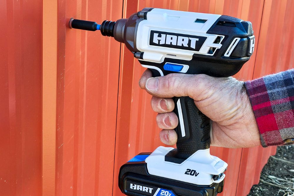 A person using a Hart Tools drill/driver kit to remove a lug nut from metal siding.