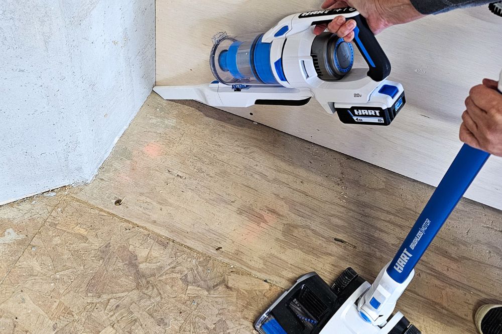 A person using the Hart cordless stick vacuum to get dust and dirt from the corner of a work area.