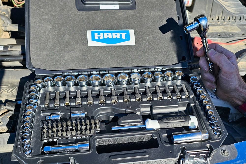 The Hart Tools mechanics tool set on a car's engine with its lid open and a person holding one of the included wrenches.
