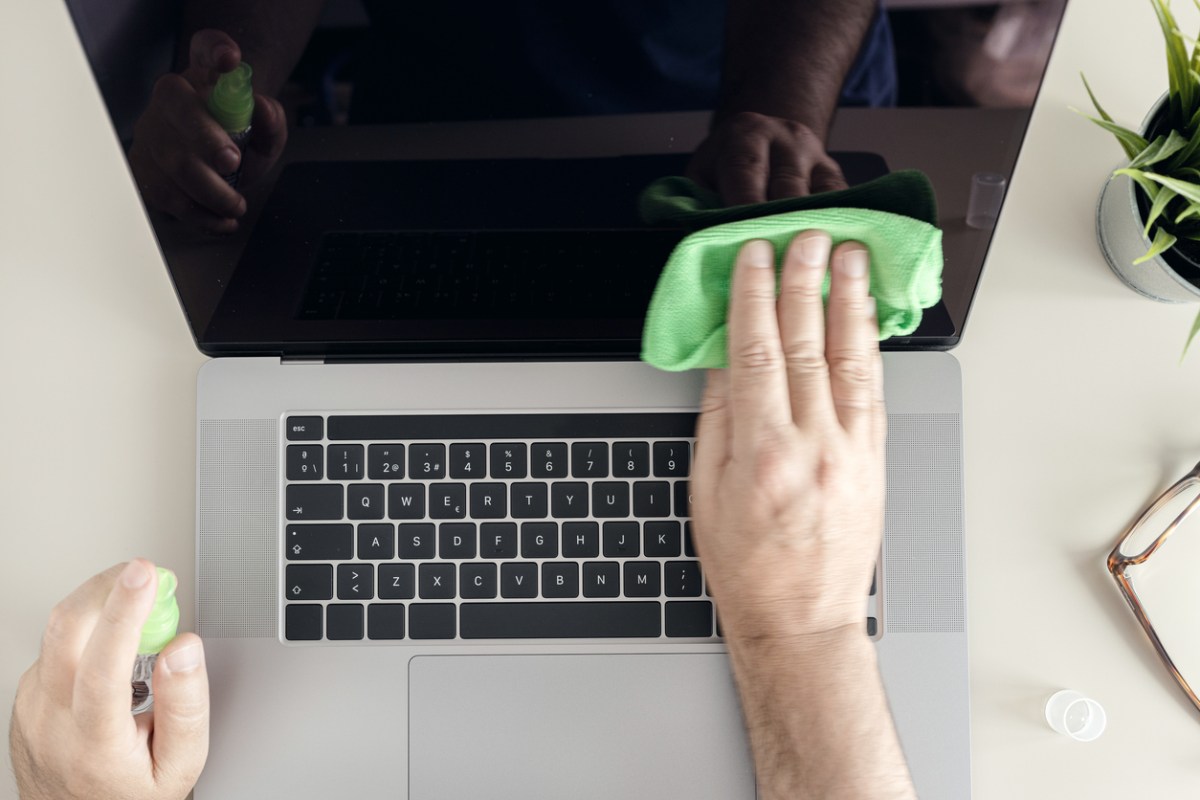 A man cleaning a MacBook laptop screen with a small green microfiber cloth.