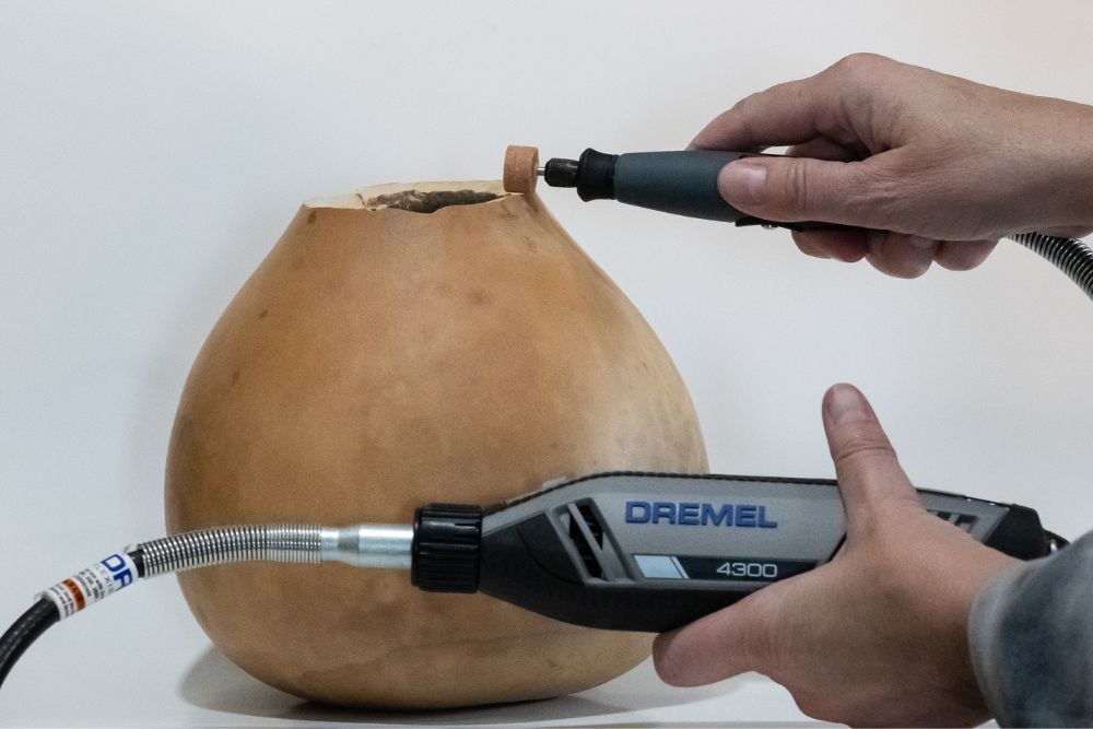 Person using Dremel 4300 to cut the top off of a dried light brown gourd
