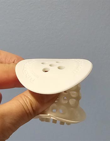 Person squeezing the base of white tubshroom silicone hair catcher for bath