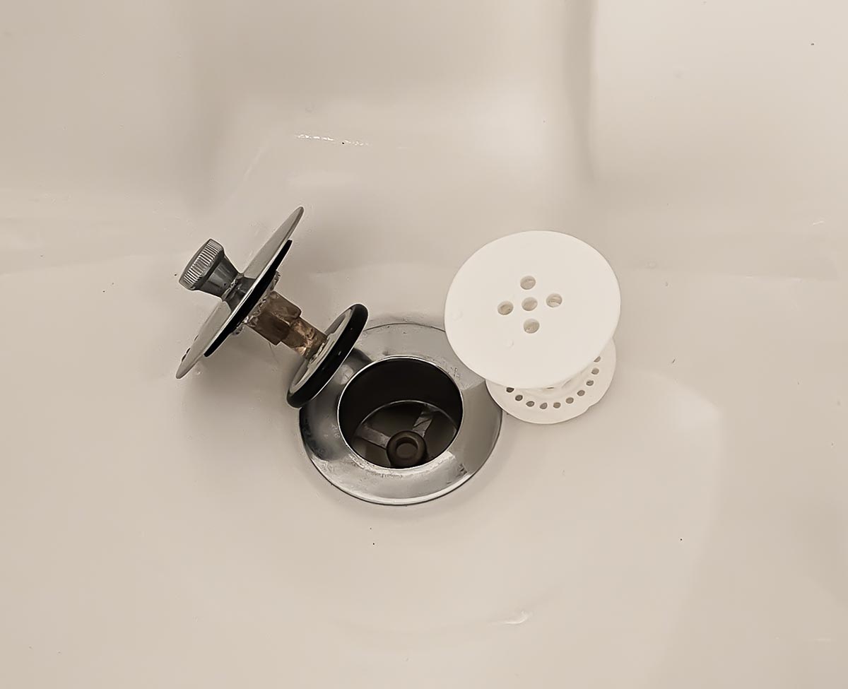 white tubshroom silicone hair catcher for bath next to drain and bath plug