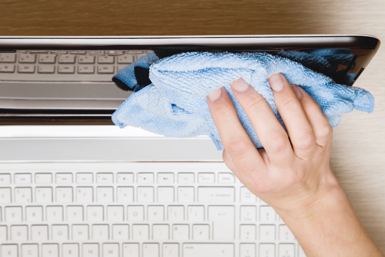 A woman wiping dust off of her laptop with a thick blue microfiber cloth.