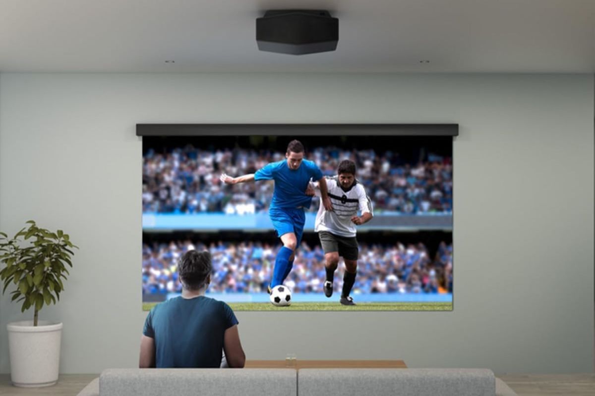 A person sitting on their couch while the best home theater projector plays a soccer game on the living room wall.