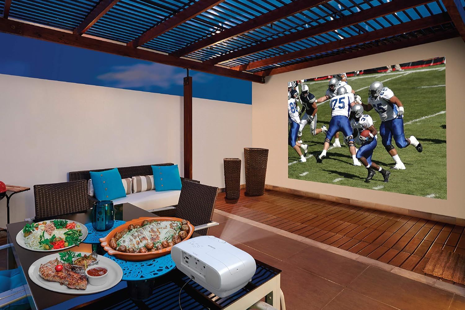The Best Home Theater Projector set up under a pergola and projecting a football game against a patio wall.