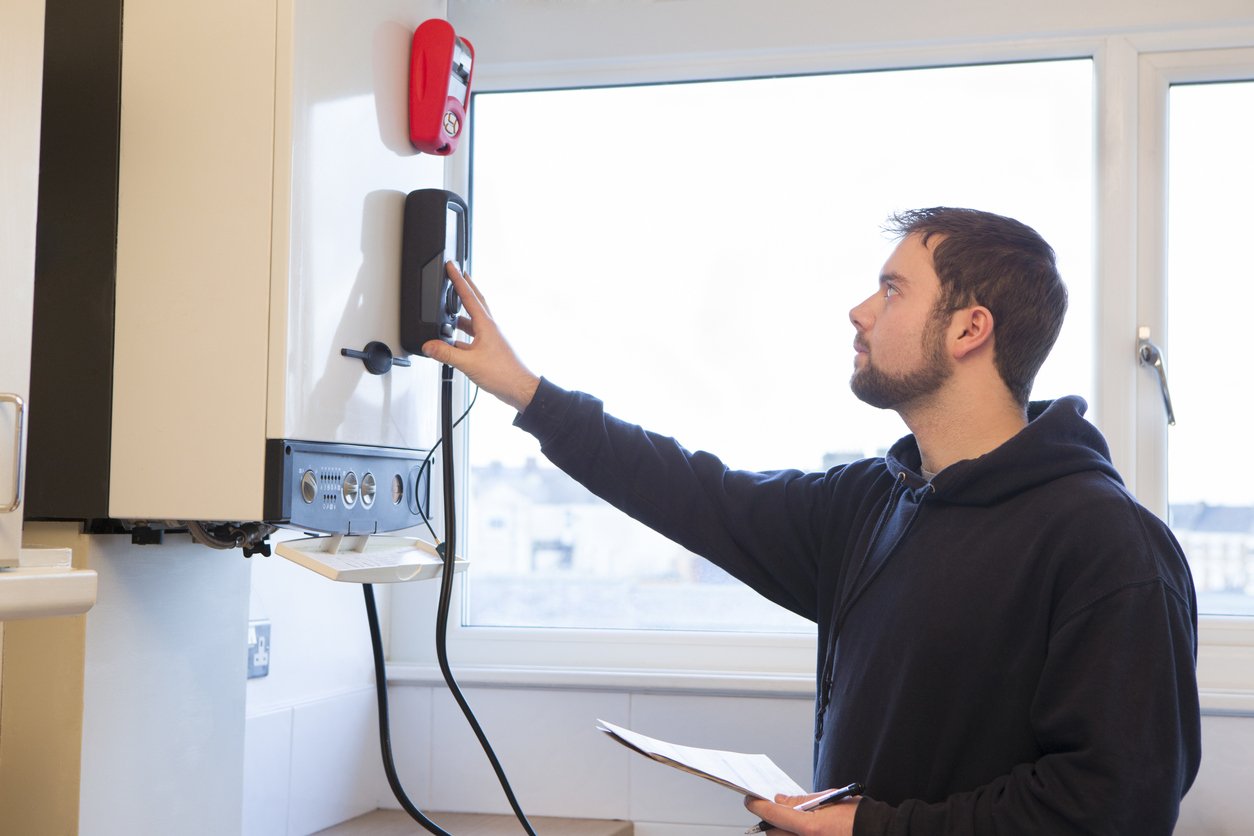 A young male engineer is standing checking the gas central heating boiler in a domestic home