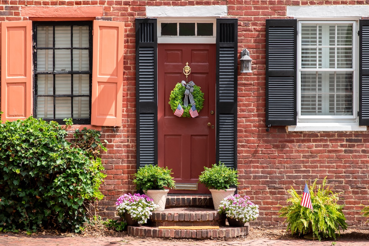 Colonial-style brick home with classic black shutters and a wreath, decorated for July 4.