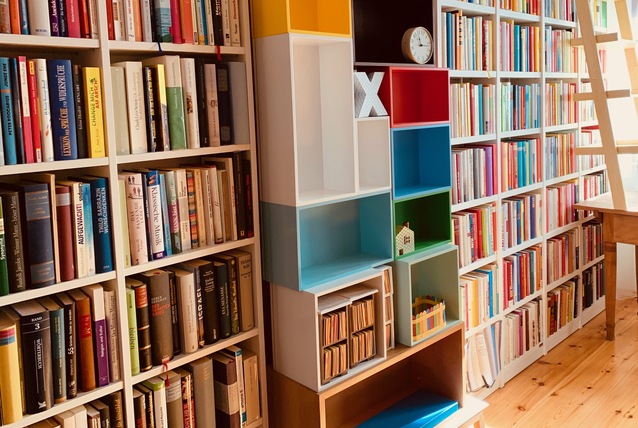 Colorful-books-line-rows-of-bookshelves-with-colorful-bins-in-the-center.