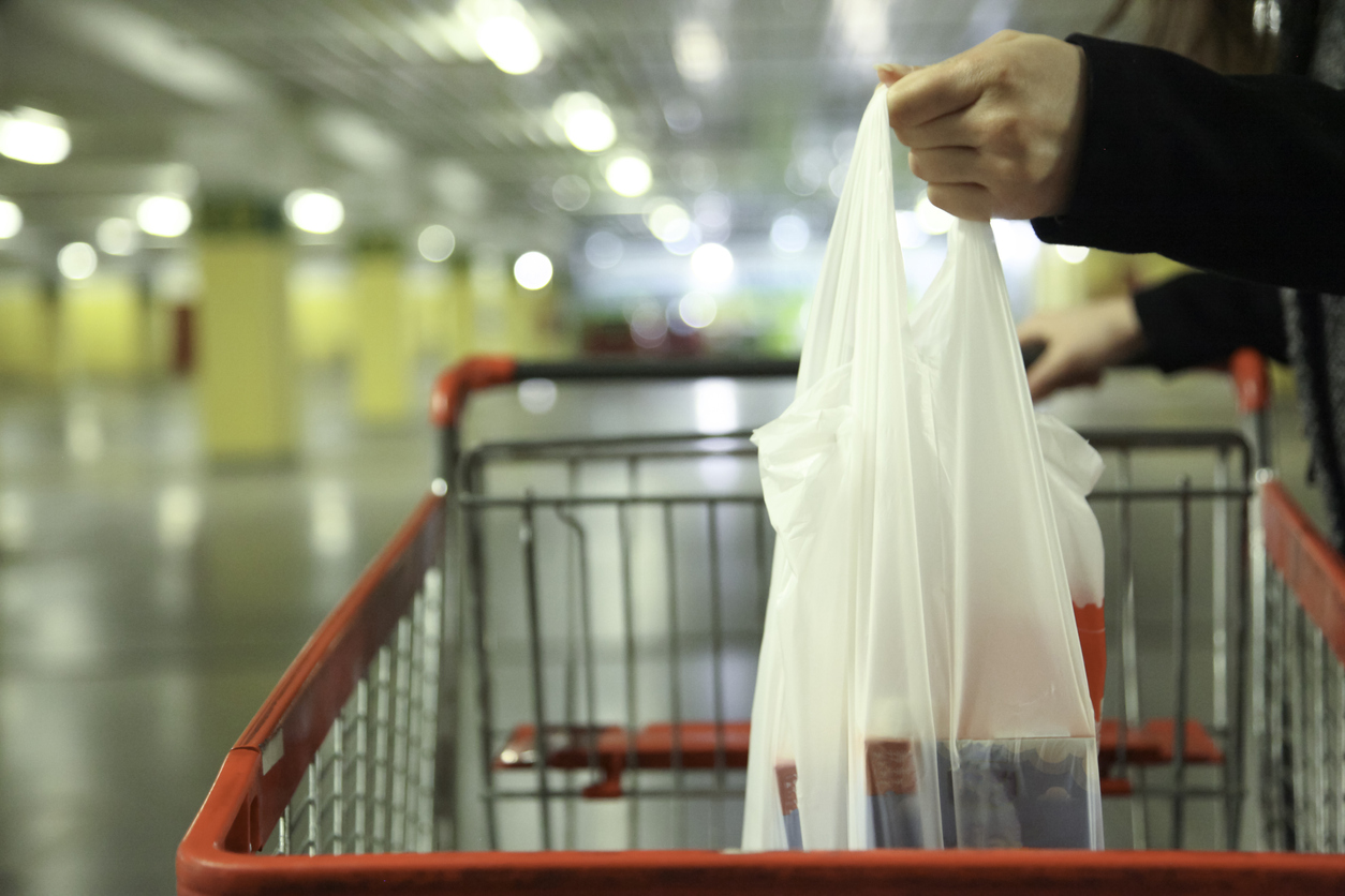 A plastic bag full of groceries being placed in a shopping cart.