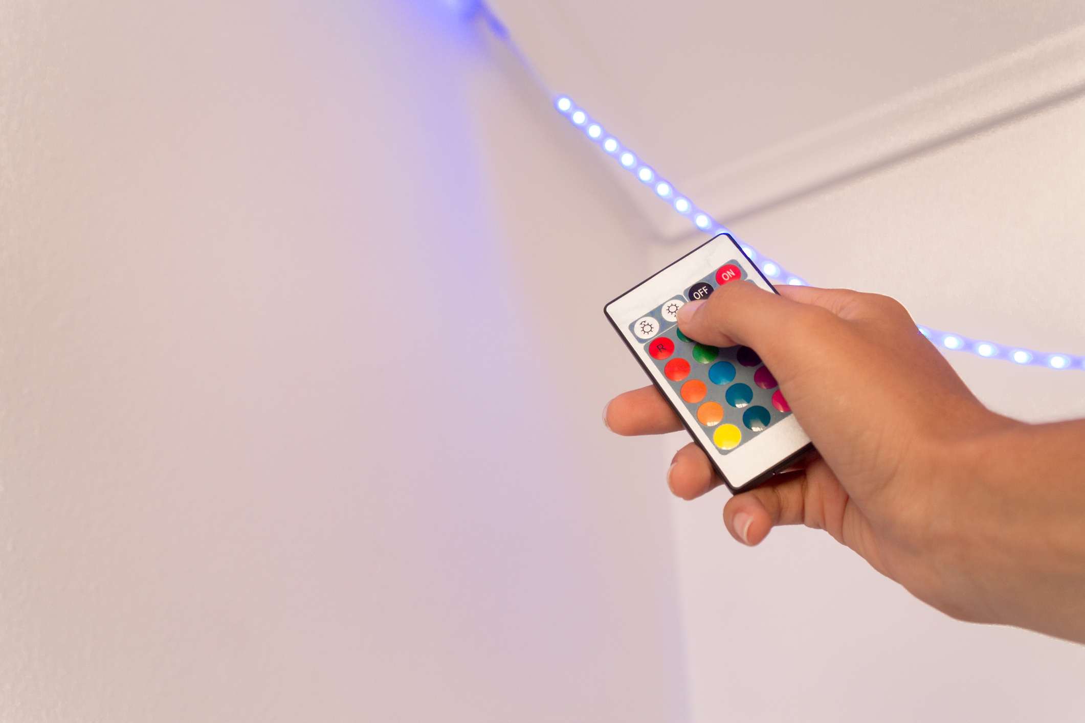 Hand holding a LED strip remote control on a white background, LED lights on and blue color of RGB LED strip pressing the remote control of the RGB LED lights