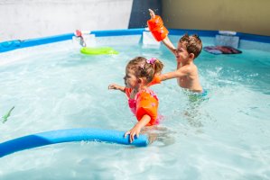 A boy and a girl are playing in swimming pool, excited because summer is here.