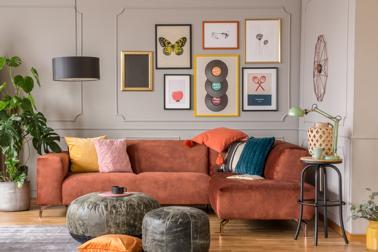 A-gallery-wall-of-art-hangs-above-a-rust-colored-sofa-in-an-eclectic-living-room.