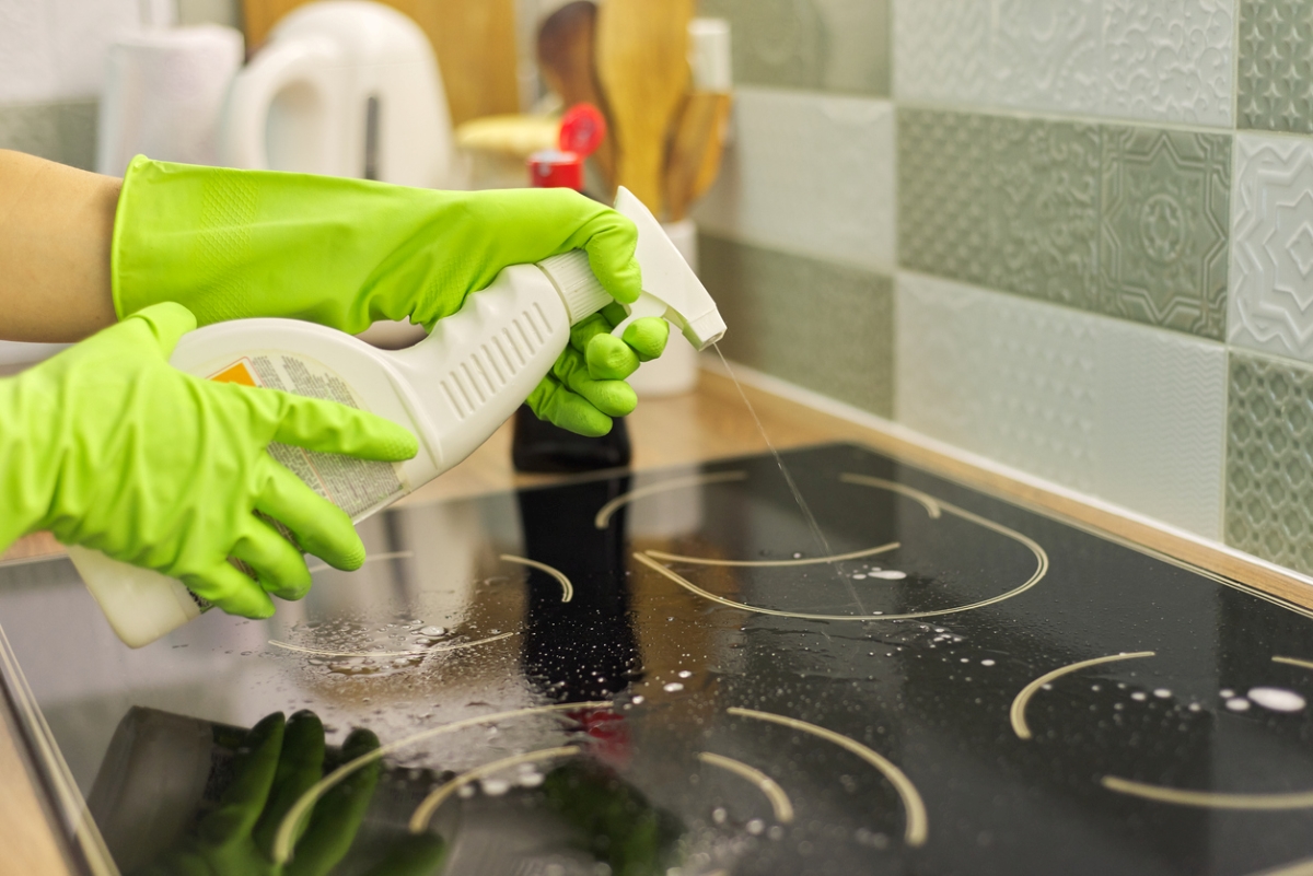 Green gloved hands spraying induction top.