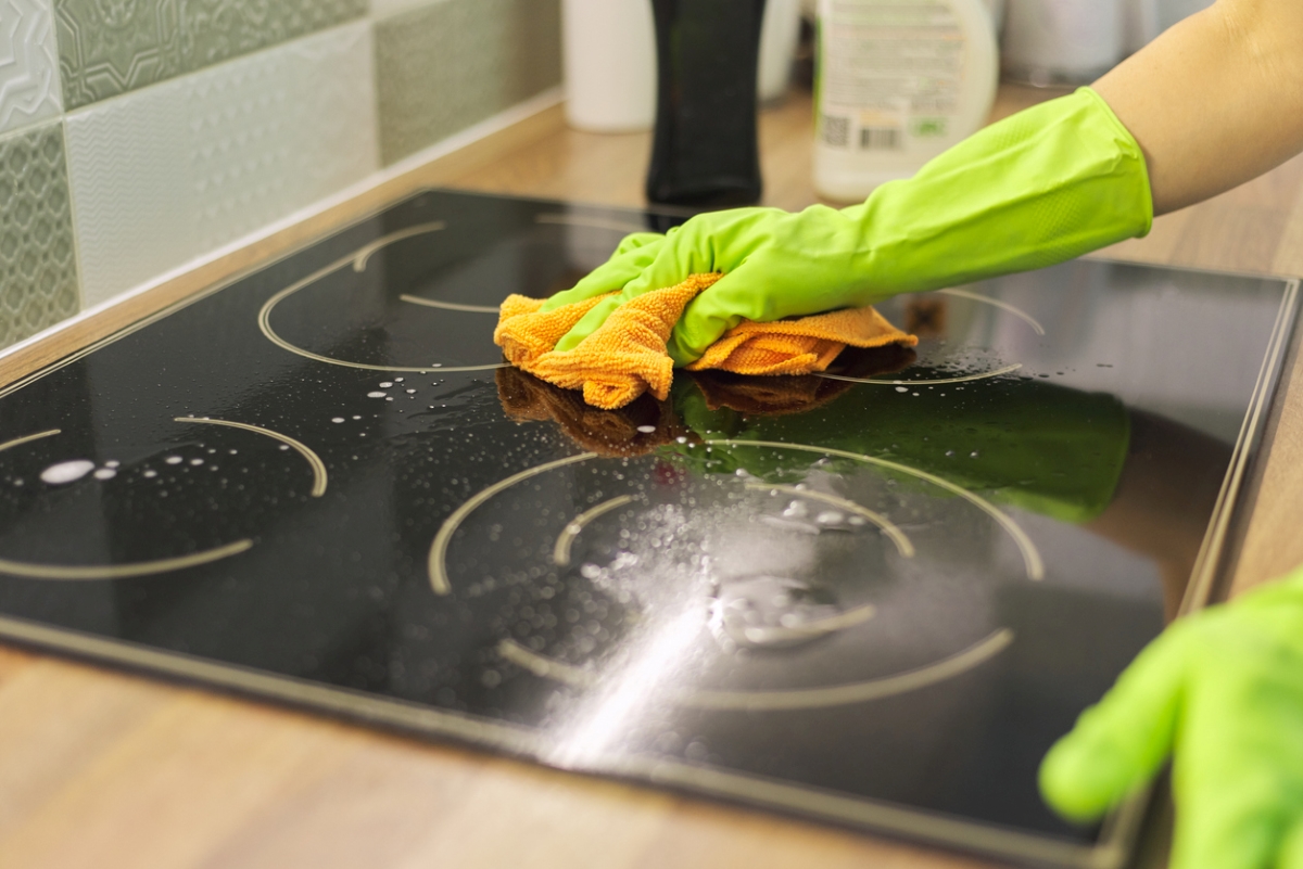 Green gloved hands using microfiber cloth on induction cooktop.