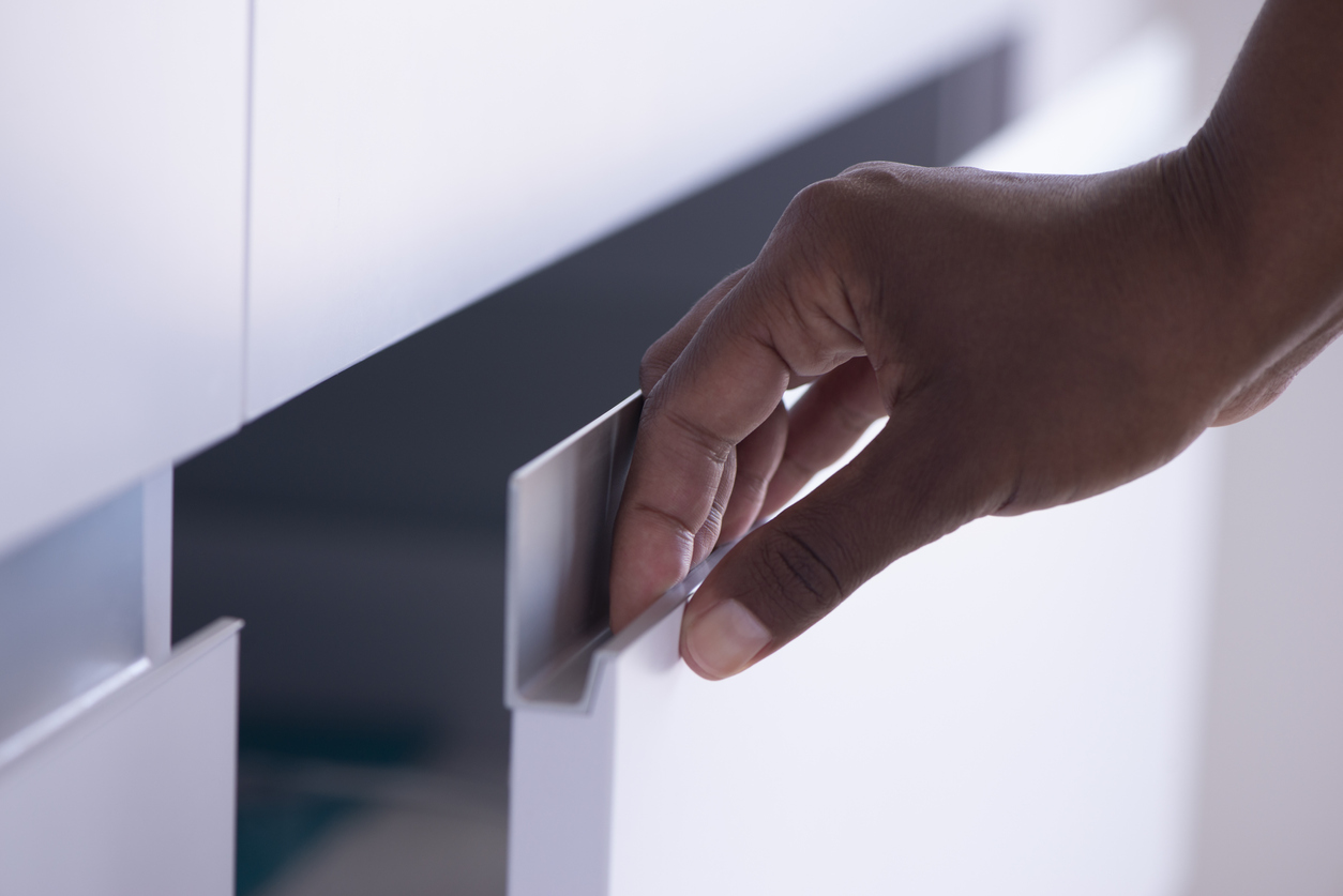 Close up image of female's right-hand opening / closing a cabinet door, touching, holding, pulling a drawer door aluminum handle.