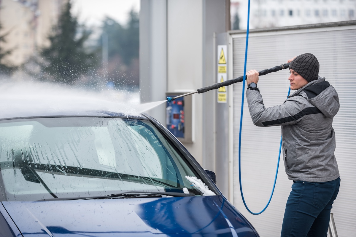 A person using a self-serve car wash to wash a car in winter.
